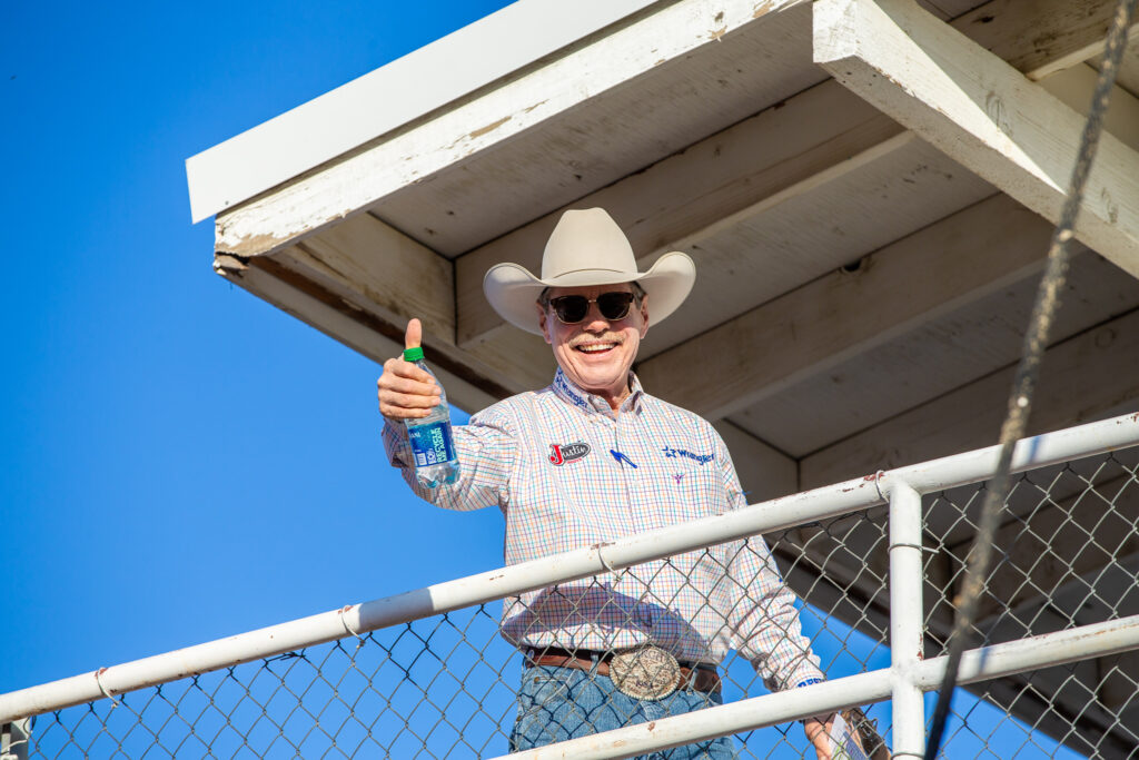 Cowboy, rodeo announcer, looking down from above with a large smile, cowboy hat and western shirt giving the camera a thumbs up.